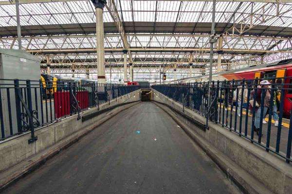 Looking down a ramp between two platforms at Waterloo Station in London. The scene is brightly lit by the light pouring in through the glass roof and there is the promise of something...